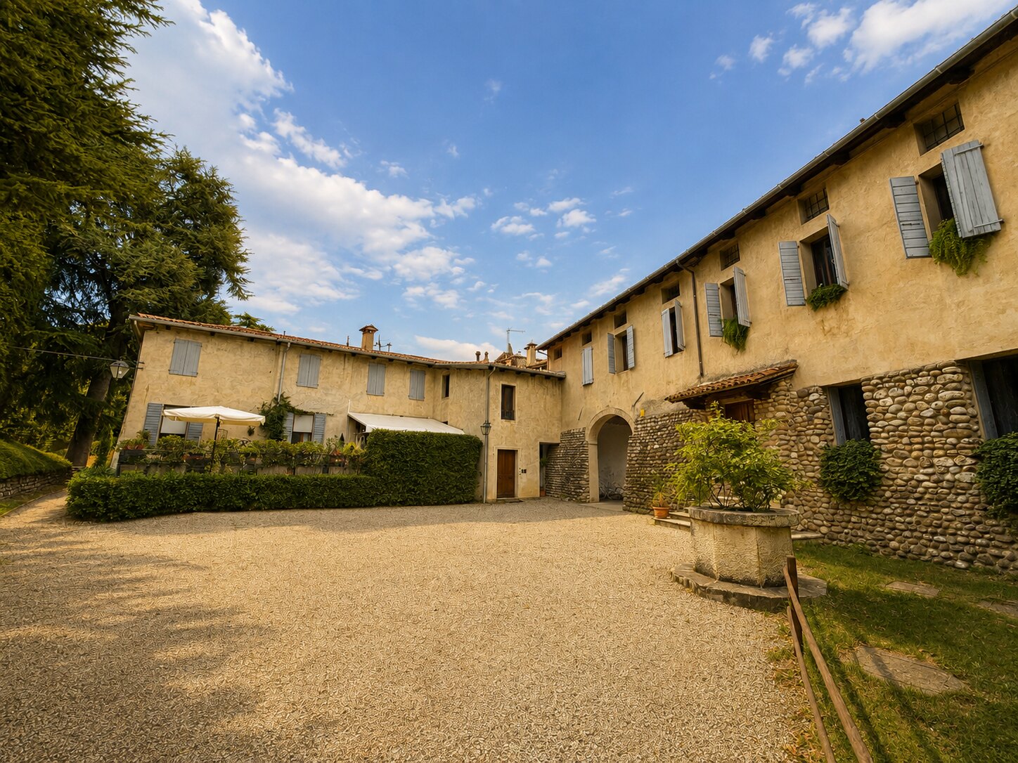 Cortile in ghiaia di Villa Giolai con edifici ocra e persiane azzurre