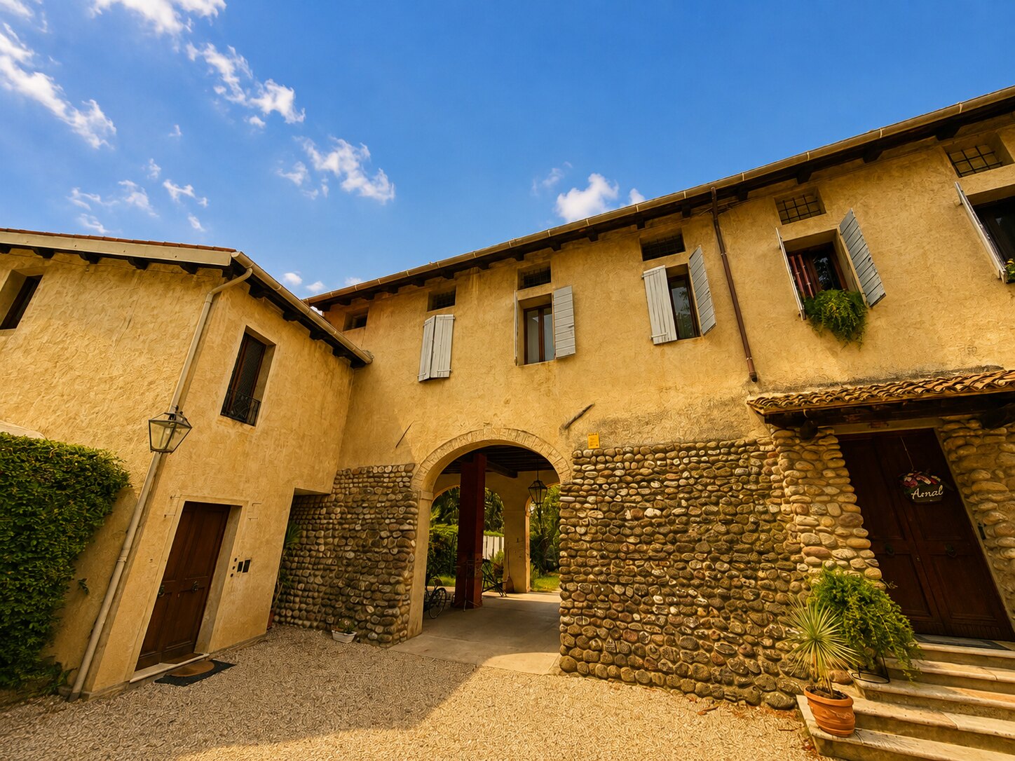 Facciata di Villa Giolai con arco in pietra, intonaco ocra e cortile in ghiaia