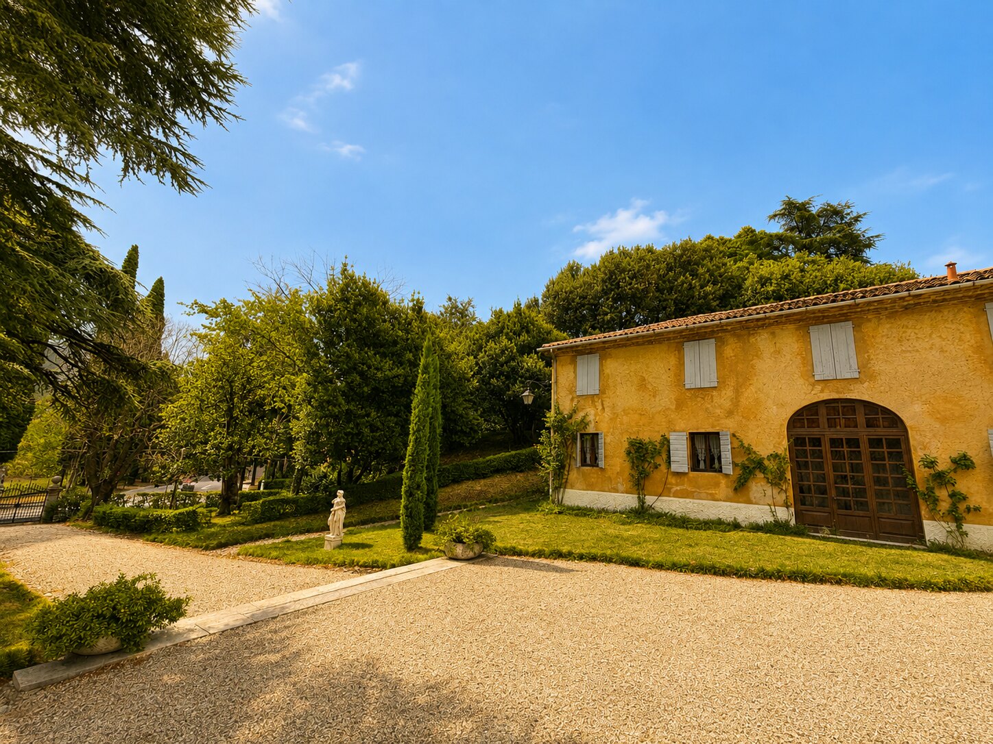 Facciata di Villa Giolai sul giardino con prato, cipressi e statua classica