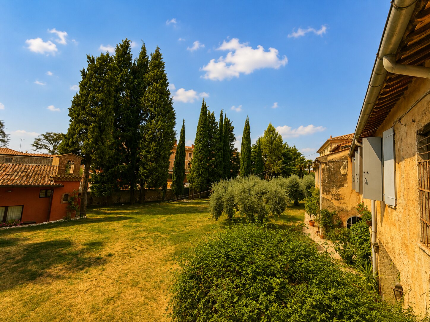 Parco interno di Villa Giolai con prato, cipressi e ulivi tra gli edifici