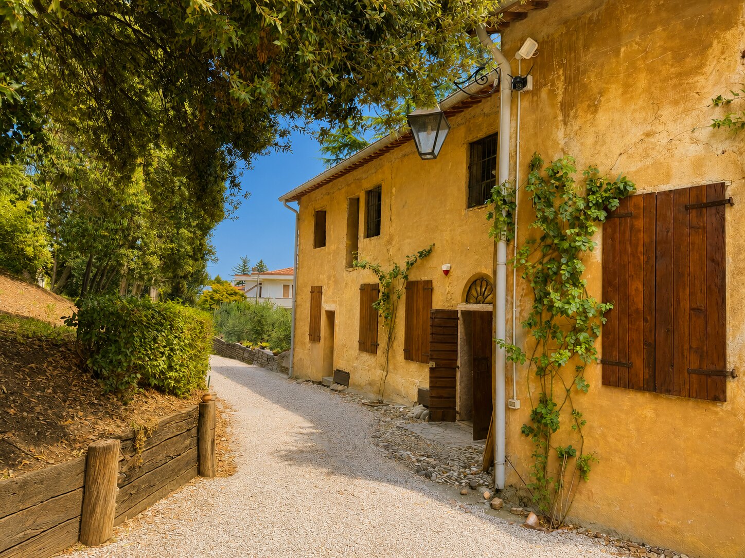Viale in ghiaia lungo la facciata ocra di Villa Giolai con persiane in legno
